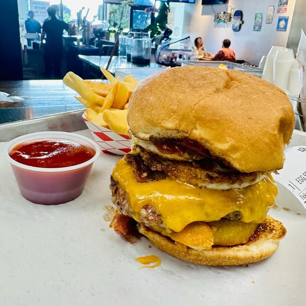 A M2 Burger with cheese, bacon, and fried egg, served with fries and ketchup.