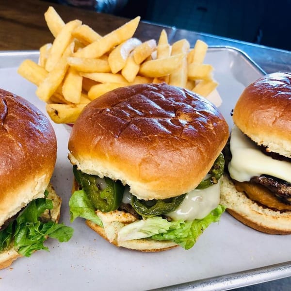 Three M2 Burger sliders with lettuce, cheese, and peppers, served with a side of golden fries.