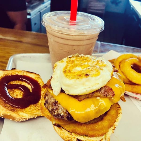 M2 Burger with fried egg, bacon, cheese, onion rings, and a chocolate milkshake.