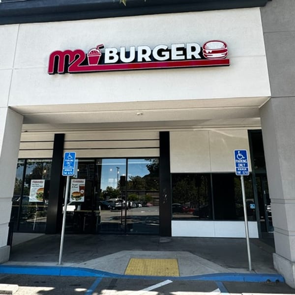 The M2 Burger restaurant exterior with its red and white logo, glass doors, and accessible parking signs.