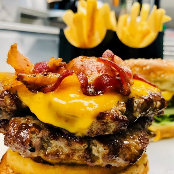 Close-up of a M2 Burger with melted cheese, crispy bacon, and waffle fries in the background.